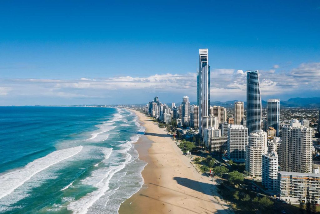 Aerial view of a coastal city skyline with tall skyscrapers adjacent to a sandy beach and blue ocean waves.