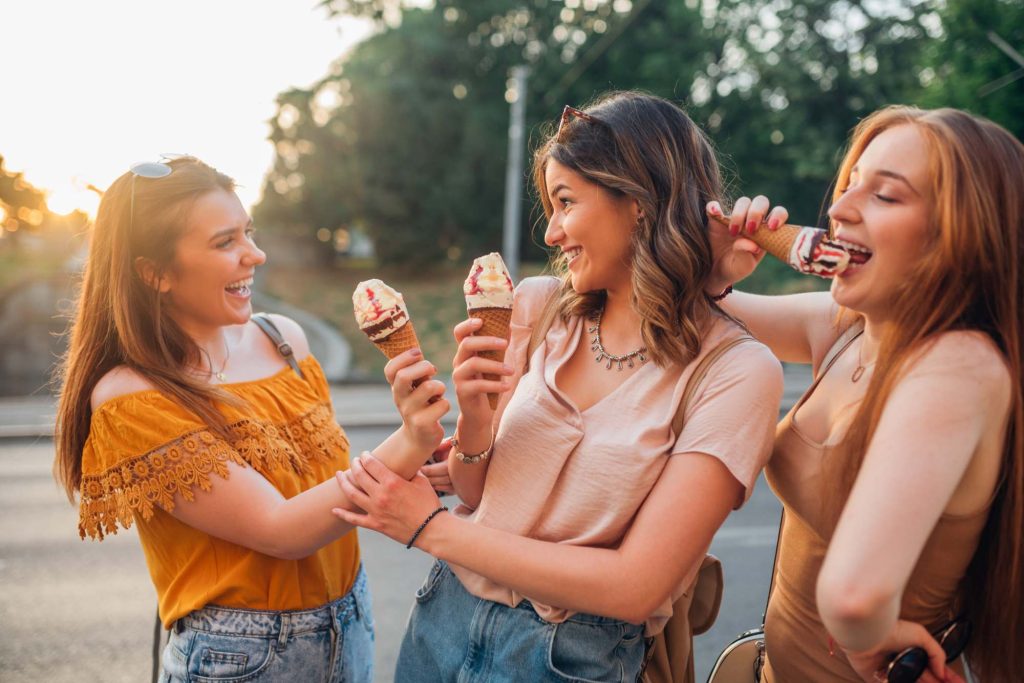 Three women enjoying ice cream cones outdoors, smiling and laughing together.