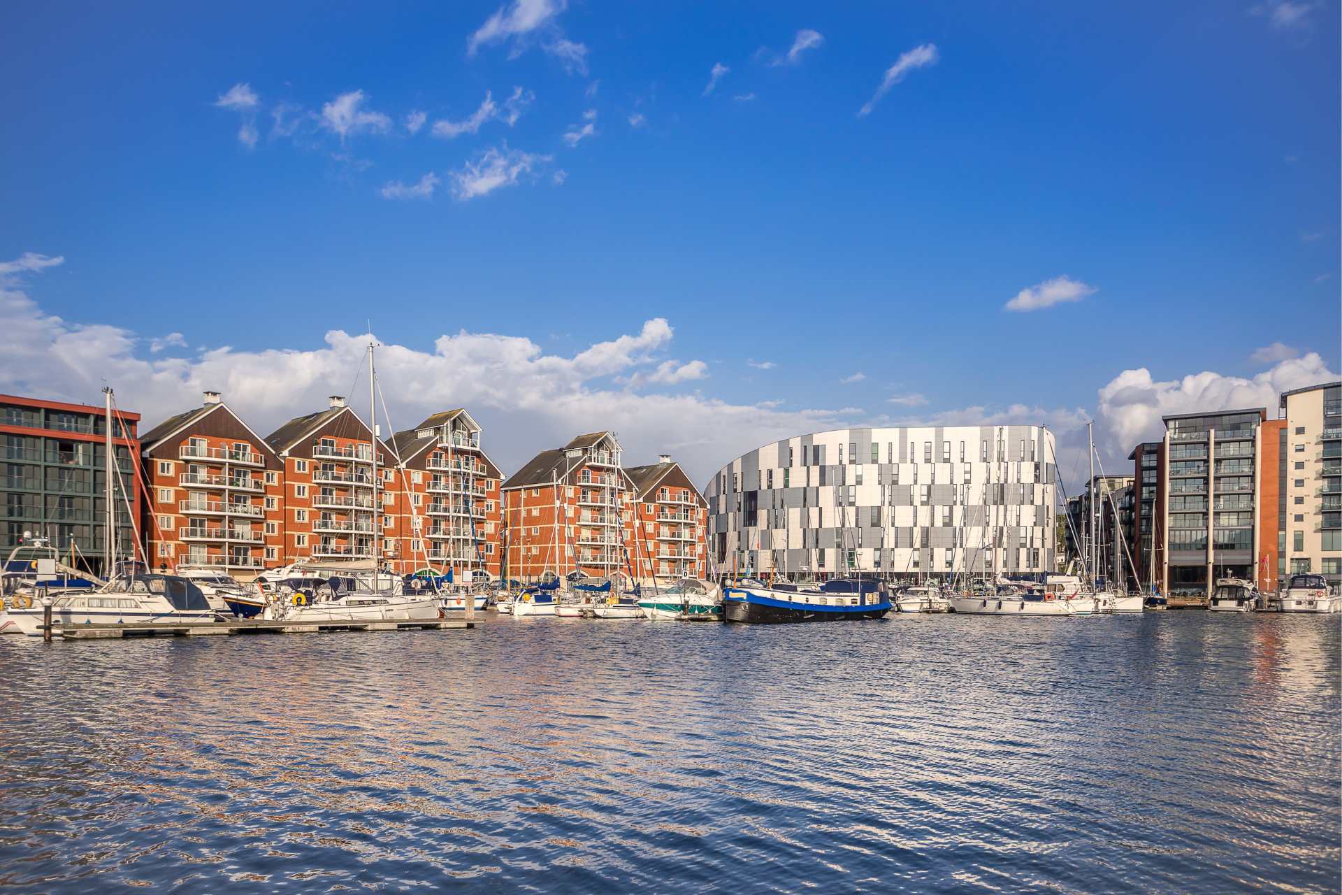 A scenic waterfront view featuring modern buildings and moored boats under a clear blue sky.